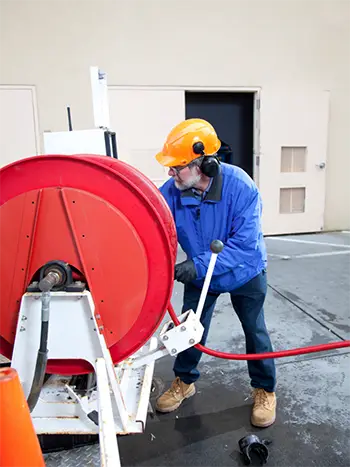 Professional plumber performing hydro-jetting drain cleaning with industrial hose and safety gear.