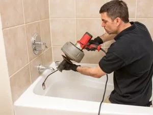 Professional plumber using a drain auger to clear a clogged bathtub drain.